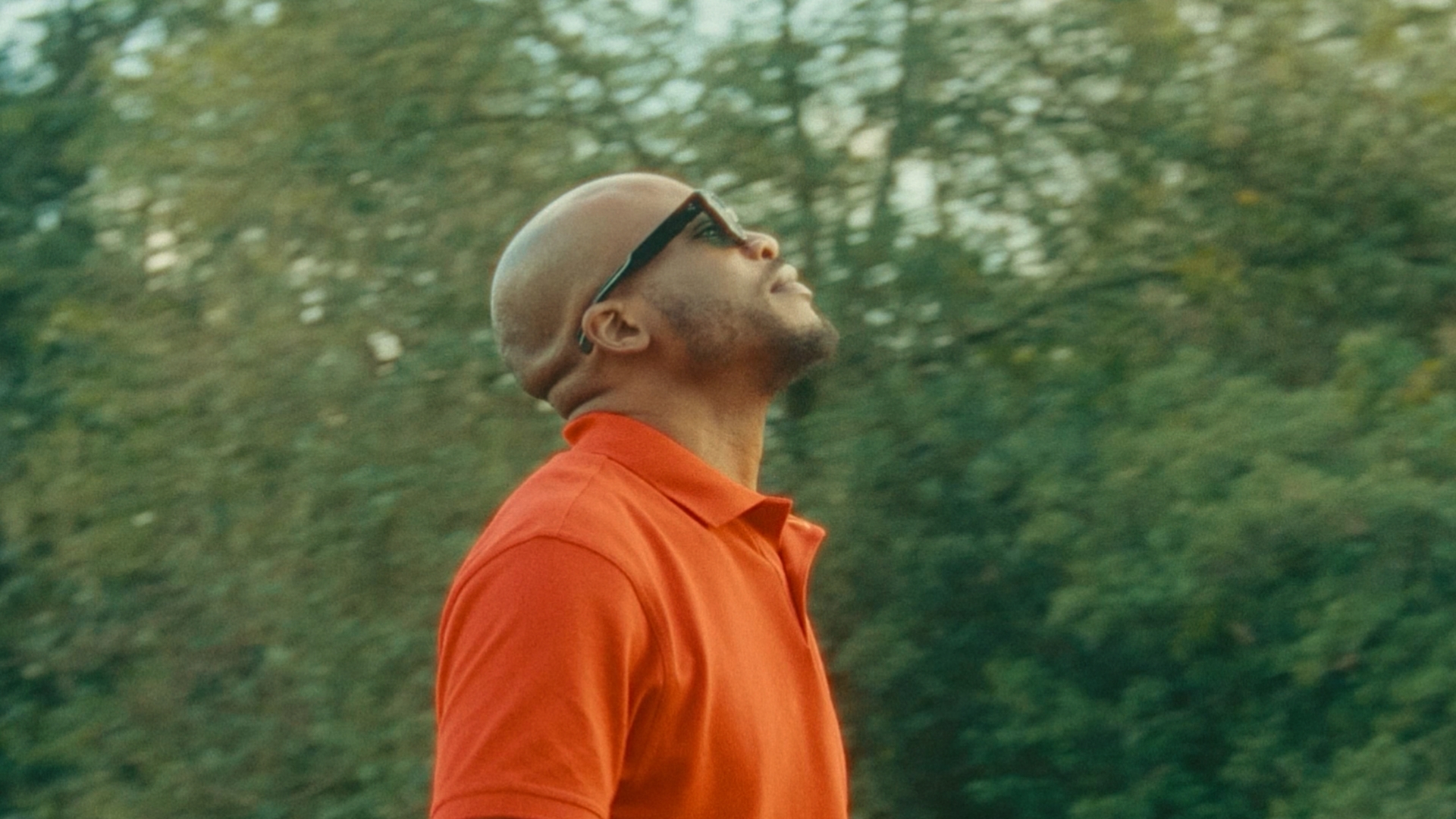Man stood in the park with his sunglasses on staring at the sky