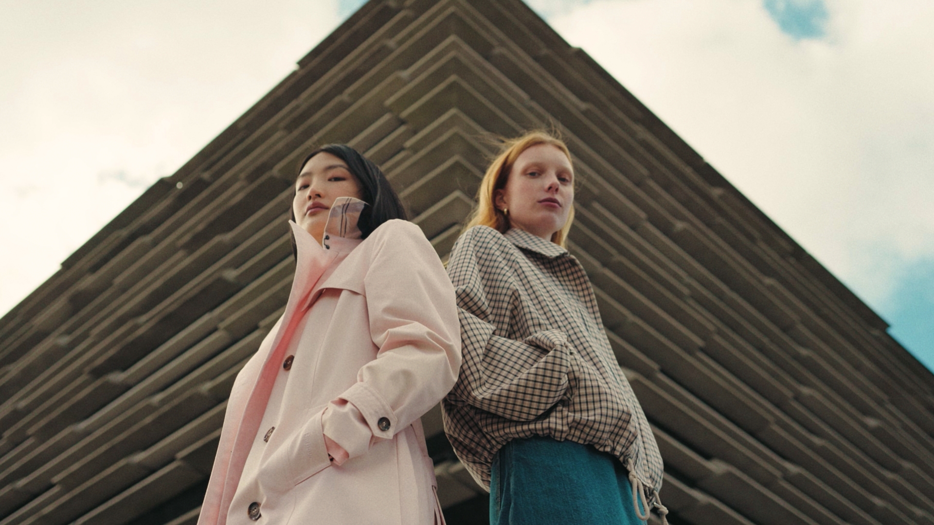 Two women stood back to back in front of a pyramid like structure
